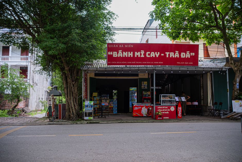 Street vendor shop in Hanoi selling Bánh Mì Cay and Trà Đá under a shady tree.